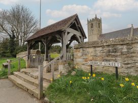 A timber lychgate with stone steps and a stone wall behind it with daffodils in front and a church tower in the background at Church View in Welford-On-Avon