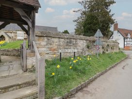 A stone wall with a church street sign and yellow flowers along the roadside near a wooden gate and a half-timbered house at Church View in Welford-On-Avon
