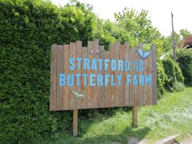 A wooden sign with blue text reading Stratford Upon Avon Butterfly Farm surrounded by green bushes