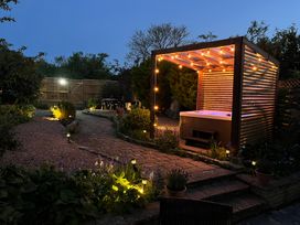 A garden with a pathway leading to a hot tub under a wooden pergola with string lights at Church View in Welford-On-Avon