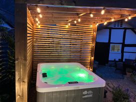 An outdoor hot tub with green light under a wooden pergola with string lights by a patio at Church View in Welford-On-Avon