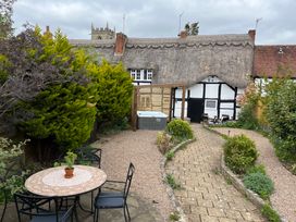 A backyard garden with a round table and chairs a hot tub and a thatched roof cottage at Church View in Welford-On-Avon