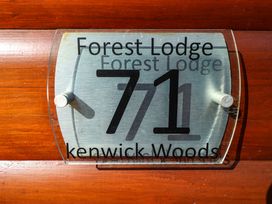 A wooden wall with a metal and glass house number sign showing 71 at Forest Lodge Kenwick Woods
