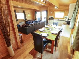 A dining table set for four with black chairs next to a kitchen and a living area with black leather sofas in a wooden cabin at Forest Lodge in Kenwick Woods