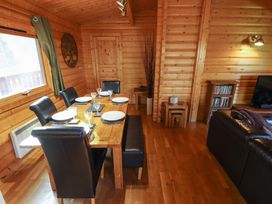 A dining area with a wooden table set with plates and glasses surrounded by black chairs and bench in a wooden cabin at Forest Lodge in Kenwick Woods