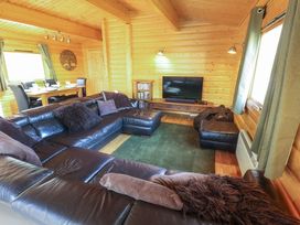 A living room with a black leather sectional sofa a wooden dining table with chairs a television on a wooden stand and wooden walls and ceiling at Forest Lodge in Kenwick Woods