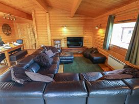 A living room with a black leather sectional sofa a television on a wooden stand and a dining table in a wooden cabin at Forest Lodge in Kenwick Woods