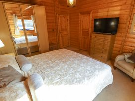 A bedroom with a bed a mirrored wardrobe a chest of drawers with a television and an armchair at Forest Lodge in Kenwick Woods