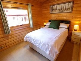 A bedroom with a double bed white bedding green pillow bedside tables with lamps and a window at Forest Lodge in Kenwick Woods