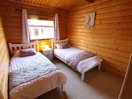 A bedroom with two single beds a nightstand with a lamp and a window at Forest Lodge in Kenwick Woods