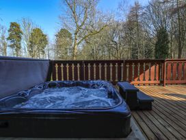 An outdoor hot tub with bubbling water on a wooden deck surrounded by trees at Forest Lodge in Kenwick Woods