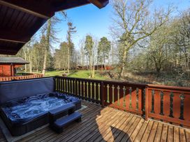 An outdoor wooden deck with a hot tub and railing overlooking trees and grass at Forest Lodge in Kenwick Woods