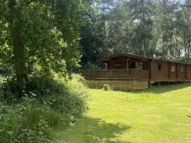 A log cabin with a deck in a forested area at Forest Lodge Kenwick Woods