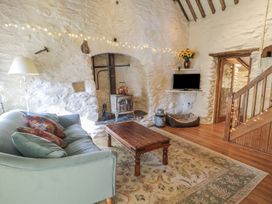 A living room with a sofa and wooden coffee table in front of a stone fireplace with a stove and a TV mounted on the wall at Old Ty'n Y Wern in Rhosygwalia near Bala