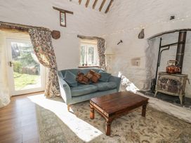 A sitting area with a blue sofa and pillows a wooden coffee table and a wood stove in a room with white stone walls at Old Ty'n Y Wern in Rhosygwalia near Bala