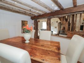 A dining area with a wooden table, white chairs, and a vase with flowers at Old Ty'n Y Wern in Rhosygwalia near Bala