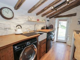 A kitchen with wooden countertops, a washing machine, a sink, a dishwasher, shelves with kitchen items, a wall clock and a glass door at Old Ty'n Y Wern in Rhosygwalia near Bala