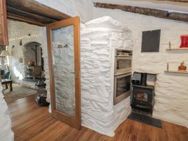 A kitchen with a wood stove oven and a wood burning stove visible through an open wooden door at Old Ty'n Y Wern in Rhosygwalia near Bala