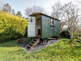 A green shepherds hut with an open white door and wooden steps on a gravel patch in a garden at Old Ty'n Y Wern in Rhosygwalia near Bala