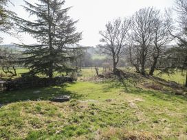 A grassy outdoor area with several trees and a stone wall in the background at Old Ty'n Y Wern in Rhosygwalia near Bala