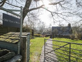 A gravel pathway leading to a stone house with a slate roof a metal gate and a wooden sign saying Old Tyn y Wern in Rhosygwalia near Bala