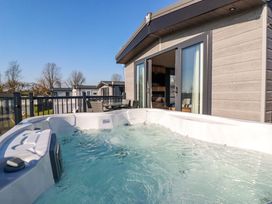 An outdoor hot tub on a deck next to a building with sliding glass doors and outdoor furniture at The Maples No 48 in Hewas Water near Sticker