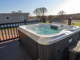 An outdoor hot tub on a wooden deck near homes and trees at The Maples No 48 Hewas Water near Sticker