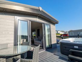 A patio with glass table and wicker chairs next to a hot tub outside a building with sliding glass doors at The Maples No 48 in Hewas Water near Sticker