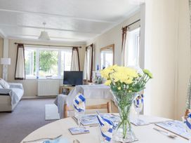 A living room with a dining area featuring a table and flowers at Lazy Days in St Merryn