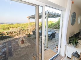 A patio area with a wooden pergola and outdoor dining table and chairs viewed through glass sliding doors at Coastmans Nest in Mawgan Porth