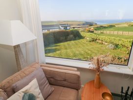 A corner of a living room with a brown sofa cushions beside a wooden table and lamp with a window showing a garden and fields at Coastman's Nest in Mawgan Porth