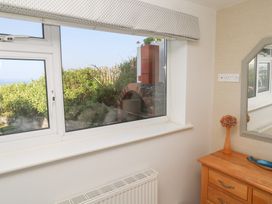 A window with a view of plants and a brick oven next to a wooden dresser with a mirror and vase at Coastmans Nest in Mawgan Porth
