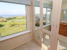 A room with mirrored wardrobe doors a wooden chest of drawers and windows overlooking a garden and countryside at Coastman's Nest in Mawgan Porth