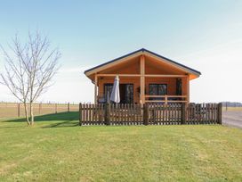 A wooden cabin with a fenced porch and a tree in a grassy yard at Alpaca Lodge in Barkston
