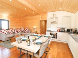 An open plan kitchen and living room with a dining table set for six and a grey sofa with red polka dot cushions at Alpaca Lodge in Barkston