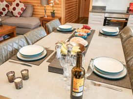 A dining table set with plates forks wine glasses a bottle of wine candles and fruit in a kitchen at Alpaca Lodge Barkston