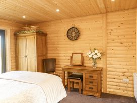 A bedroom with wooden walls and ceiling a bed a wooden wardrobe a chair a wooden dressing table with a mirror and flowers and a wall clock at Alpaca Lodge in Barkston