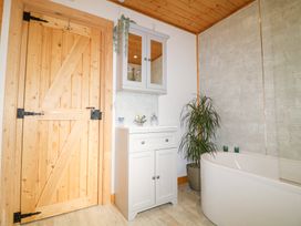 A bathroom with a wooden door white sink cabinet wall cabinet bathtub and a plant at Alpaca Lodge in Barkston
