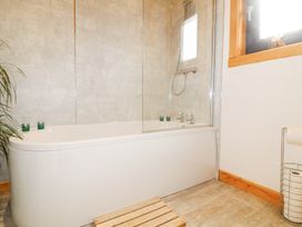 A bathroom with a bathtub a shower head candles a wooden bath mat and a window at Alpaca Lodge in Barkston