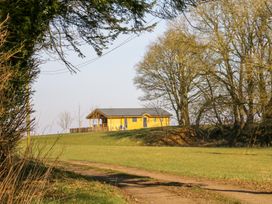 A dirt path leading to a yellow house on a grassy hill surrounded by leafless trees at Alpaca Lodge in Barkston