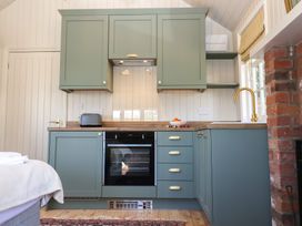 A kitchen with green cabinets a black oven a toaster a bowl of oranges and a gold faucet at The Woodshed in Tendring near Weeley