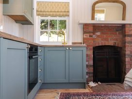 A kitchen with blue cabinets a brass faucet a brick fireplace and a window with a patterned blind at The Woodshed in Tendring near Weeley