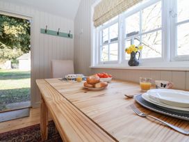 A wooden dining table with plates cups toast and a bowl of tomatoes next to a window with flowers at The Woodshed in Tendring near Weeley