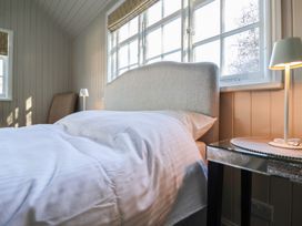 A bedroom with a bed a side table with lamp and windows at The Woodshed in Tendring near Weeley