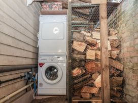A laundry area with a stacked washer and dryer next to a storage area with firewood behind wire mesh at The Woodshed in Tendring near Weeley