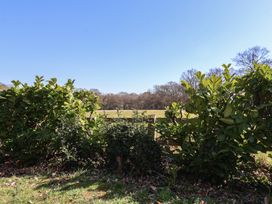 A garden with green shrubs in front of a wooden fence and open fields at The Woodshed in Tendring near Weeley