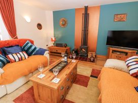 A living room with sofas with orange throws a wooden coffee table a wood burning stove and a television at Rayson Hall Barns in Ousby