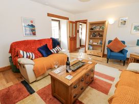 A living room with a sofa covered with orange and blue throws and a wooden coffee table with wine glasses and a bottle at Rayson Hall Barns in Ousby