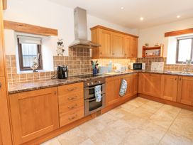 A kitchen with wooden cabinets, a stainless steel oven and range hood, a microwave, two small windows, and tiled floor at Rayson Hall Barns in Ousby