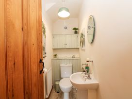 A small bathroom with a toilet sink a round mirror wooden door and wall cabinets at Rayson Hall Barns in Ousby